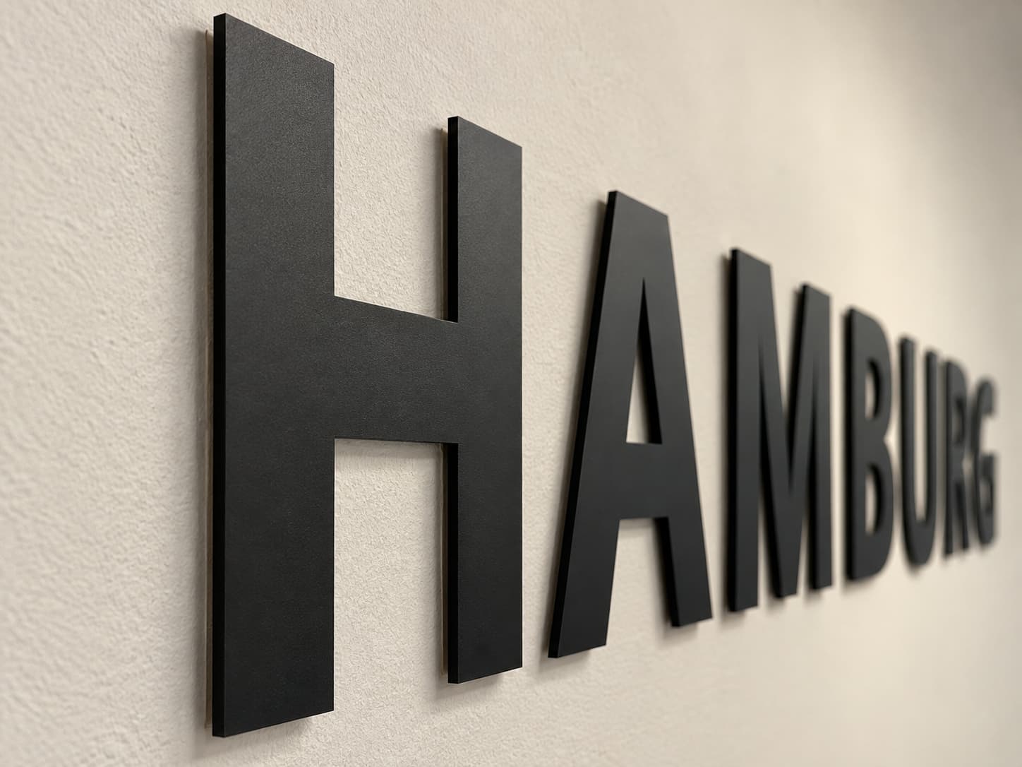 Dreidimensionaler schwarzer Schriftzug HAMBURG an einer hellen Wand
